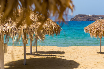 Fototapeta na wymiar Palm frond umbrella on the yellow sand beach, blue water, island in the background