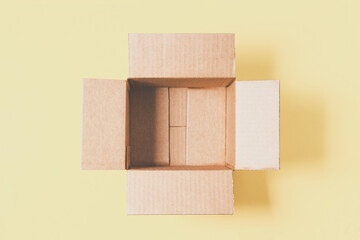 One empty open cardboard box on pastel yellow background. Top view, copy space