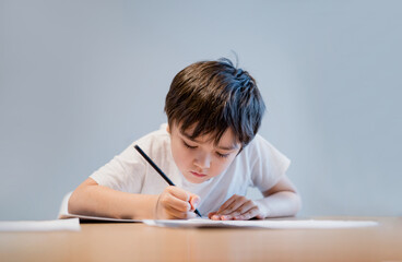 Kid holding pencil writing on white paper, Child boy is drawing, Portrait of school kid doing homework alone, Elementary homeschooling, New normal life style children learning at home
