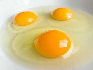 Three bright yellow raw chicken eggs in a white bowl.