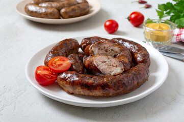 Juicy homemade baked sausage on a plate with mustard and fresh tomatoes.