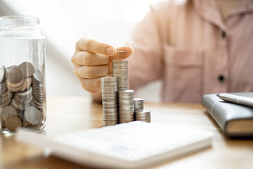 A woman is stacking coins in a row and a jar with a lot of coins, she is doing an income statement and dividing the money for saving. Concept of saving money and investing it to grow money.
