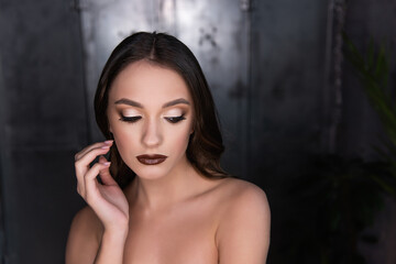 Close up beauty portrait of a brunette girl with brown eyes, professional evening make-up, dark lipstick, smoky eyes in a gold corset. A festive image for a party. Silver dark background. Copy space