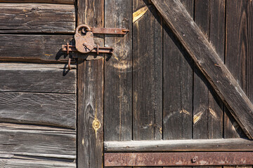 The wall of an old wooden barn built from hand-hewn pine logs. Old wooden door reinforced with a wrought iron strip closed with an iron bolt and a vintage rusty lock