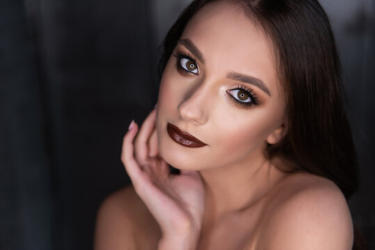 Close up beauty portrait of a brunette girl with brown eyes, professional evening make-up, dark lipstick, smoky eyes in a gold corset. A festive image for a party. Silver dark background. Copy space