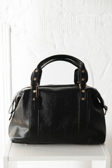 black leather bag with handles on a white background in front. gold jewelry