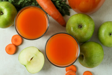 Glasses with juice and ingredients on white textured background