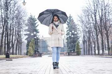 Portrait of a brunette girl with an umbrella walking in cloudy and rainy weather