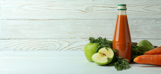 Bottle of juice and ingredients on white wooden background