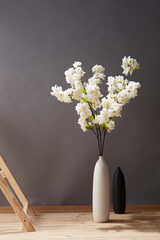 Still life: flowering branches of white sakura in white vase near wooden ladder and empty black...