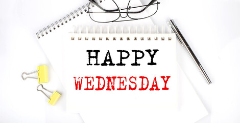 HAPPY WEDNESDAY text on the notebook with pen,clips and glasses