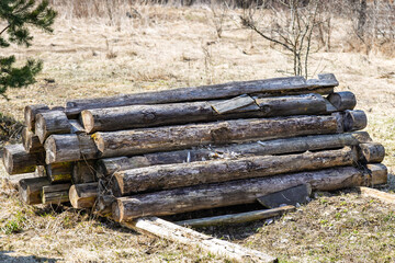 A pile of old rotten logs piled on the ground in the open air. Logs from an old disassembled house piled in a heap