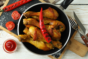 Concept of delicious eating with pan of roast chicken drumsticks on white wooden table