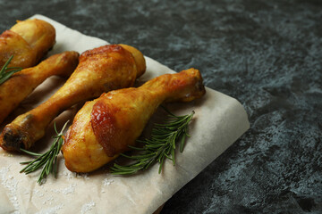Board with roast chicken drumsticks on black smokey background