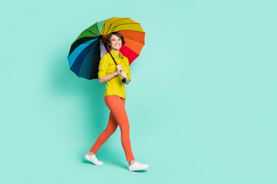 Full length body size photo of girl smiling under colorful umbrella isolated bright teal color background