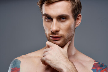 Fototapeta na wymiar portrait of young man with tattoos on gray background and beautiful face model cropped view