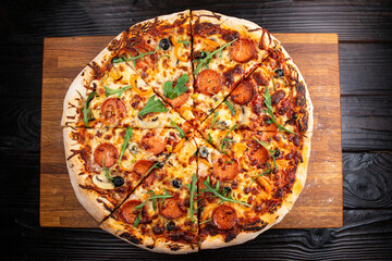 Colorful appetizing fresh hot pizza with salami and oregano cut into slices on an oak board against a dark wood table background