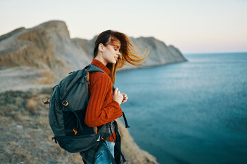 woman in a sweater with a backpack walks in nature in the mountains near the sea