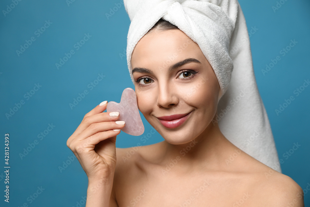 Canvas Prints Beautiful young woman doing facial massage with gua sha tool on blue background