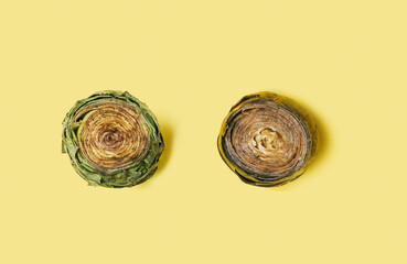 Modern concept of two organic artichokes cleaned up and trimmed, one raw fresh and second one cooked. Flat lay composition on light yellow background.