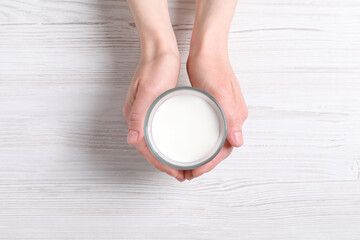 Woman holding glass of milk at white wooden table, top view