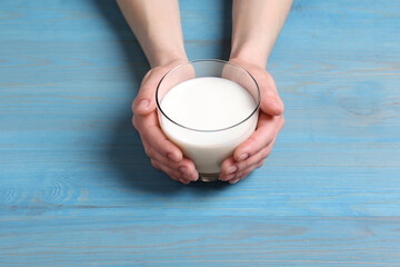 Woman holding glass of milk at light blue wooden table, closeup