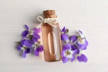 Beautiful wild violets and essential oil on white wooden table, flat lay. Spring flowers