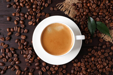 Cup of hot aromatic coffee and roasted beans on wooden table, flat lay