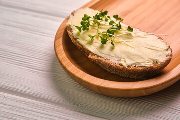 Spreading tasty butter onto slice of bread with knife on plate, closeup
