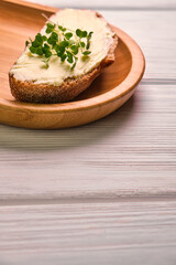 Spreading tasty butter onto slice of bread with knife on plate, closeup