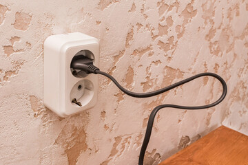 Plug in a double outlet on a white plaster background in a modern room interior