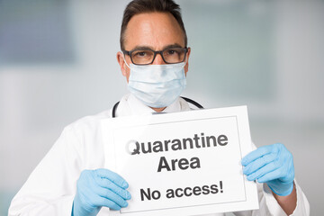 Doctor with medical face mask and medical gloves showing quarantine sign in front of a restricted...