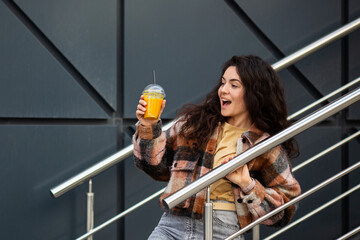 Young stylish woman with juice cup standing over gray background. Portrait of a smiling woman with...