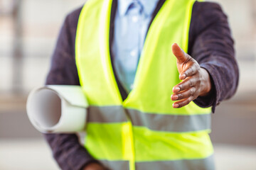 Fototapeta na wymiar Handsome construction worker in protective helmet and vest are extending hand to shake. Architect with an open hand ready for handshake - concept about agreement, partnership and win-win situation
