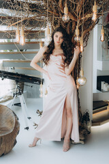 Beautiful, stylish, and elegant girl brunette, model, with makeup and curly hair in a peach-colored silk dress for a magazine photoshoot in fashion style.