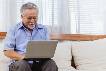Happy healthy Asian senior elderly man working on computer at home. Retired grandfather enjoy...