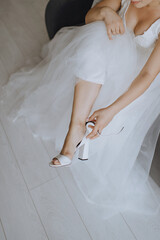 morning of the bride, getting ready, the bride in a wedding dress puts on wedding shoes, legs close-up