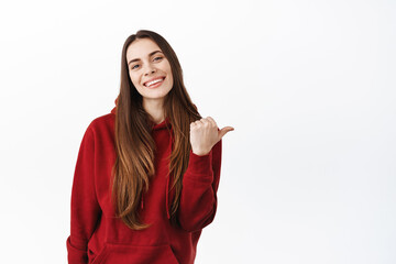 That way. Smiling gorgeous woman with long hair pointing thumb right, showing advertisement aside on copy space, give recommendation, praise product, standing over white background