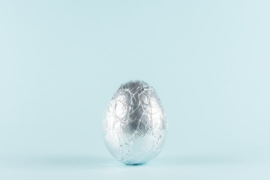 Easter egg wrapped in a silver foil against pastel blue background. Easter minimal concept. Creative Happy Easter or spring layout.