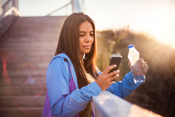 Sports woman using fitness app. African sports woman standing on the stairs holding bottle of water...