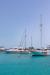 Fototapeta na wymiar White motor and sailing yachts moored in the azure waters of the Red Sea in the harbor of Hurghada. Clear blue skies echo the color of the sea