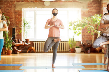 fitness, meditation and health care concept - group of people wearing black face protective masks for protection from virus disease doing yoga in tree pose at studio