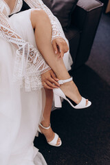 morning of the bride, getting ready, the bride in a wedding dress puts on wedding shoes, legs close-up