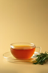 Organic Rosemary tea in glass cup with rosemary plant on beige background. Herbal tisane drink for health.