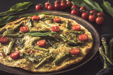 Homemade tarte flambee with green asparagus, tomatoes and pesto on a wooden plate