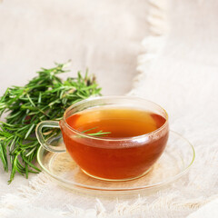  Glass of aromatic Rosemary tea with rosemary bunch on linen tablecloth. Modern Rustic style.