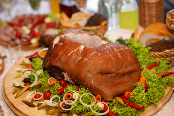 A large piece of roast pig on a wooden plate decorated with greens and salad for the holiday. Fresh fatty grilled pork meat on a wooden bowl