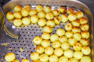 Fried round early potatoes in a metal tray laid out closely to each other. Oven-fried rice balls. Small round potato fried until golden brown.