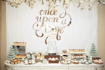 Wedding Candy Bar with a large three-story cake in a classic style. Table with sweets and desserts for guests at the holiday. White wooden table with pastries and a large cake