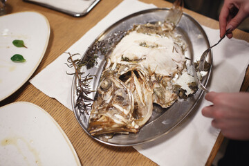 The girl cuts with a knife and fork a fresh fried dorado. Sea fish on a silver plate.